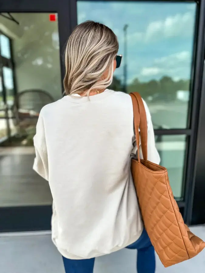 Woman wearing a casual light cardigan with a camel tote bag, showcasing the Leopard Bow Sand Graphic Cardigan style.