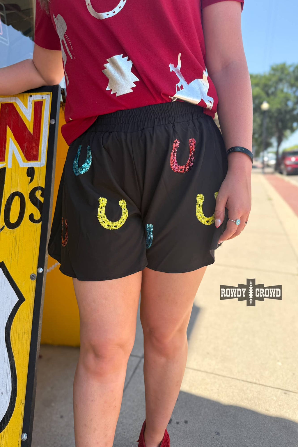 Model wearing Lucky Buck Shorts with colorful horseshoe design in vibrant yellow, red, and turquoise.