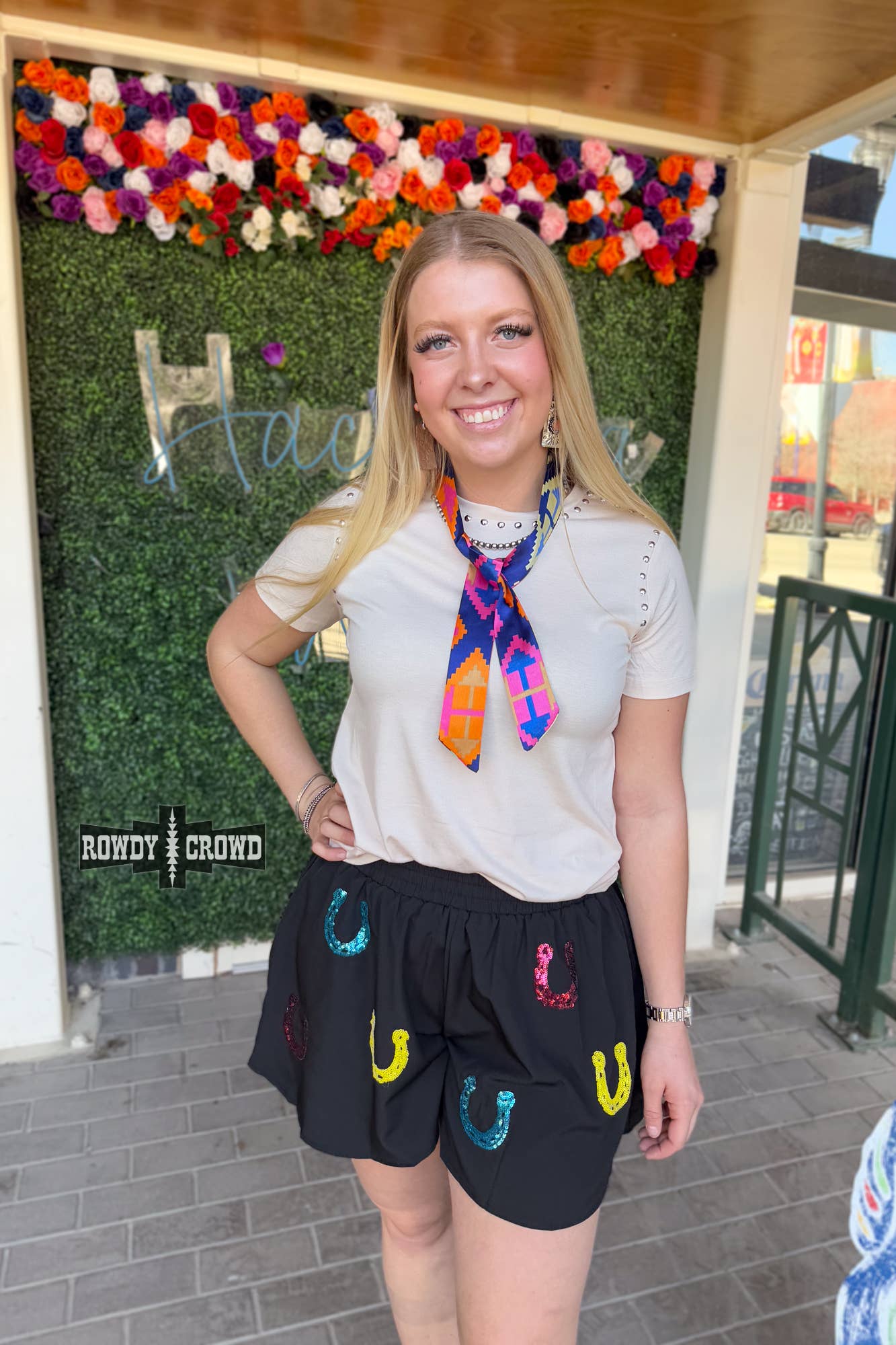 Woman wearing Lucky Buck Shorts with vibrant horseshoe designs and colorful accessories.