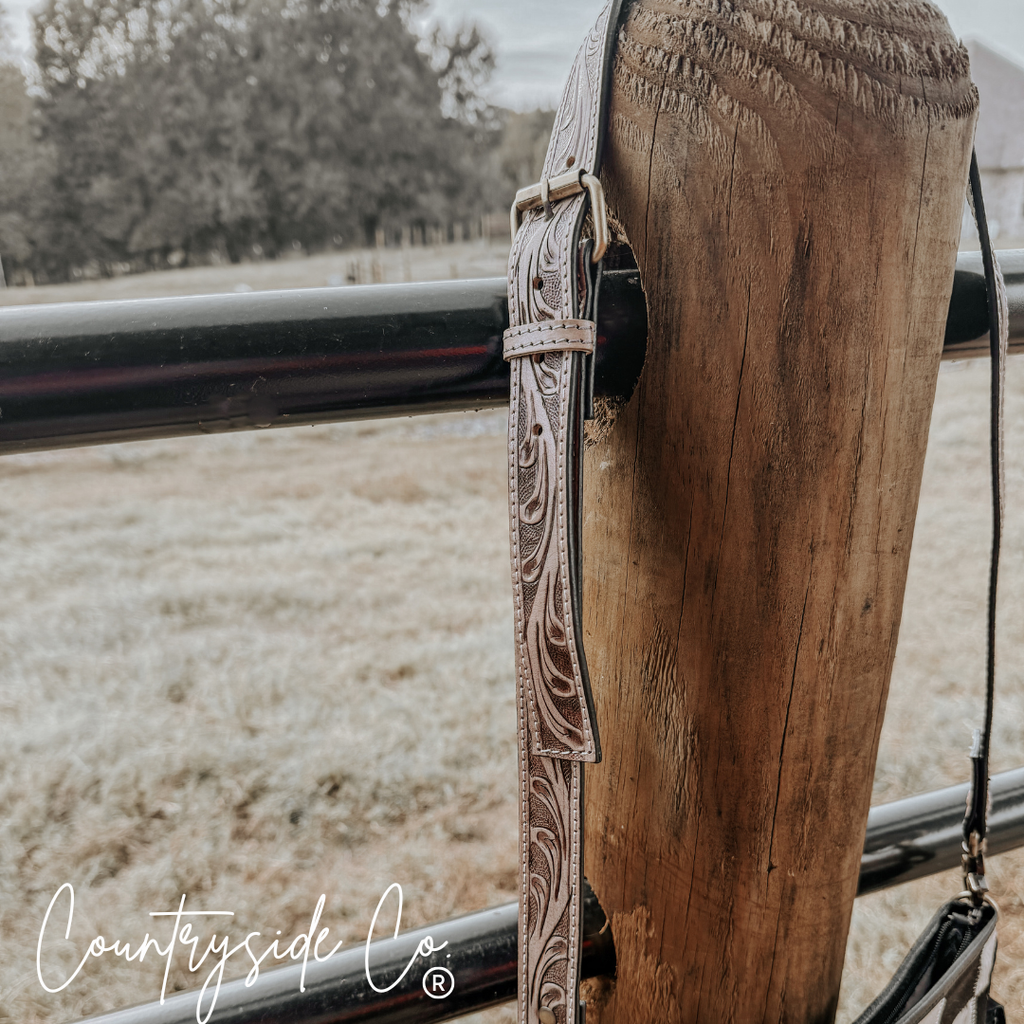 Rodeo Square Cowhide Checkered Purse showcasing a tooled leather shoulder strap on a rustic fence post.