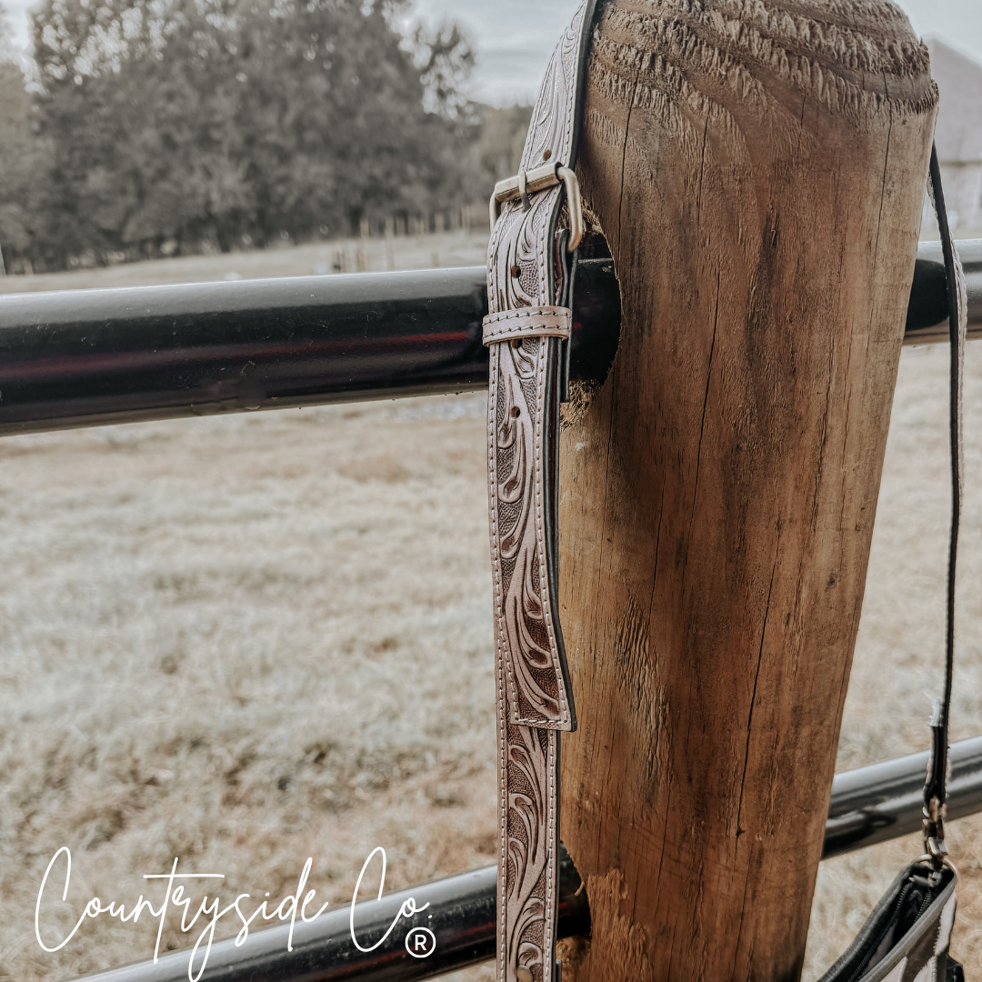 Rodeo Square Cowhide Checkered Purse showcasing a tooled leather shoulder strap on a rustic fence post.